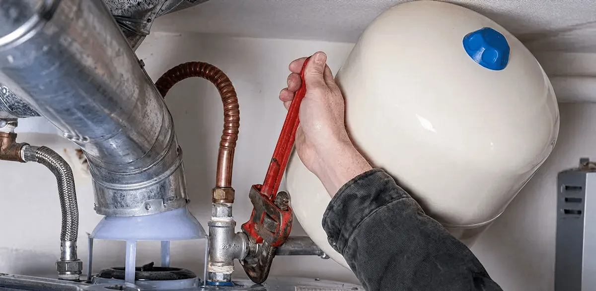 Water heater repair technician tightening plumbing connections near a tank unit in Nashville, TN